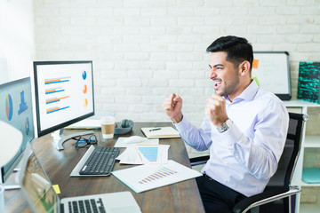 Fototapeta na wymiar Hispanic Businessman Enjoying Successful Data At Desk