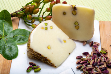 Italian provolone or provola cheese made in Sicily with tasty green Bronte pistachio nuts served on white marble plate close up