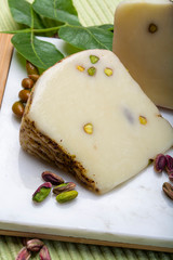 Italian provolone or provola cheese made in Sicily with tasty green Bronte pistachio nuts served on white marble plate close up