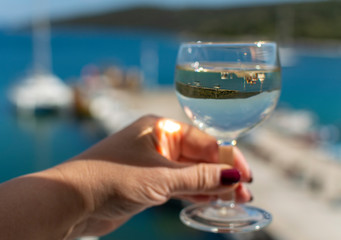 hand with glass of white wine served outside on balcony with sea view