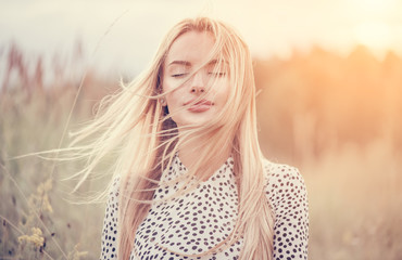 Close Up Portrait of beauty girl with fluttering white hair enjoying nature outdoors, on a field. Flying blonde hair on the wind. Breeze playing with girl's hair. Beautiful young woman face closeup.