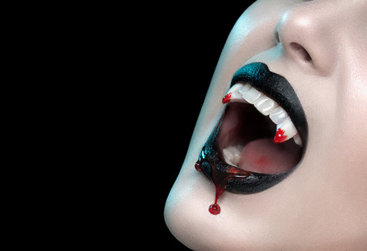 Vampire teeth with dripping blood, Woman's black bloody lips close-up. Vampire girl fangs. Fashion Halloween art design. Close up of female vampire mouth, teeth. Isolated On black background