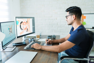 Handsome Young Male Editor Using Graphic Tablet At Desk