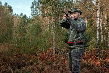 Naklejka premium Hunter man in camouflage with a gun during the hunt in search of wild birds or game on the background of the autumn forest. Autumn hunting season. The concept of a hobby, killing.