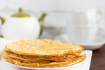 homemade freshly baked pancakes on the table and tea utensils in the background.