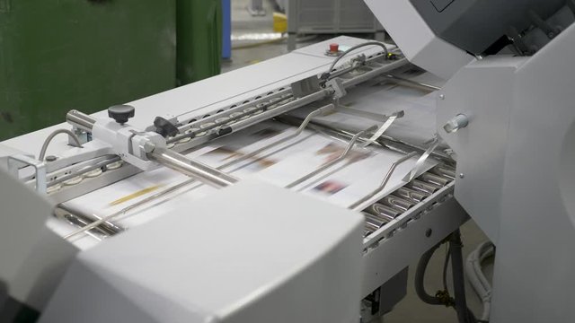 A static view of numerous sheets of printed papers moving through rollers under printing machine, at the printing house.
