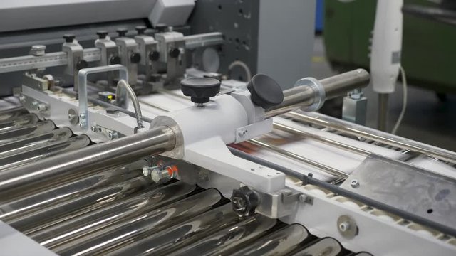 A static view of numerous sheets of printed papers moving through rollers under printing machine, at the printing house.(2)