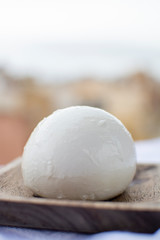 Italian mozzarella soft cheese ball served on wooden plank with yellow houses in old Italian town on background