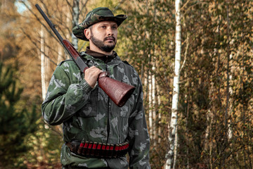 Fototapeta premium Hunter man in camouflage with a gun during the hunt in search of wild birds or game on the background of the autumn forest. Autumn hunting season. The concept of a hobby, killing.