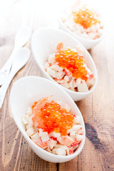 Salad with seafood and red caviar in portioned bowls on a wooden table, selective focus