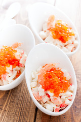 Salad with seafood and red caviar in portioned bowls on a wooden table, selective focus