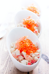 Salad with seafood and red caviar in portioned bowls on a wooden table, selective focus