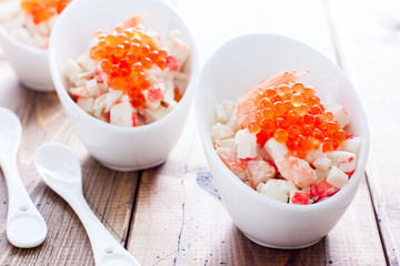 Salad with seafood and red caviar in portioned bowls on a wooden table, horizontal