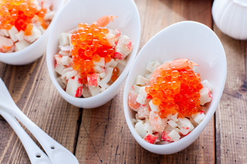 Salad with seafood and red caviar in portioned bowls on a wooden table, horizontal