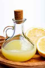 Fresh lemon juice made from ripe yellow Sicilian lemons used for cooking in glass bottle on olive wood plate