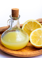 Fresh lemon juice made from ripe yellow Sicilian lemons used for cooking in glass bottle on olive wood plate