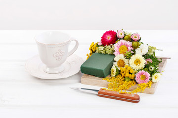 Woman shows how to make floral arrangement with summer flowers inside a ceramic cup