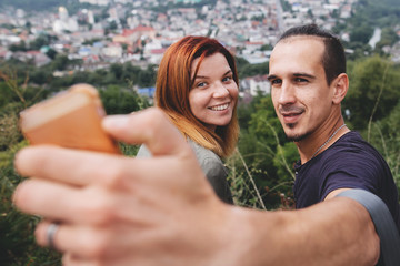 Happy hipster couple taking selfie on phone on background of beautiful view on old town building in Europe. Tourist couple smiling and making photo. Traveling in european city.