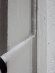 Carefully apply the white silicone sealant from the gun to the vertical  old painted wooden surface