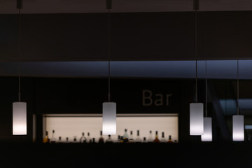 blurred backlight bottles of alcohol at bar and lamps in foreground after drinking