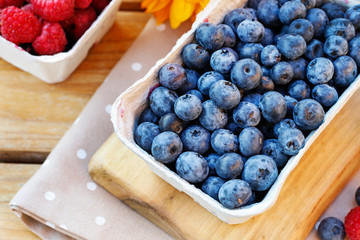 Paper box with blueberries and flowers in the background.