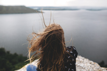 Back of hipster girl sitting on top of rock mountain with beautiful view on river. Young tourist...