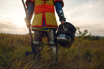 Medieval knight in armor holds axe and helmet