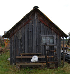 Old small fisher house with paddles and net. Head of snow woman on the bench. Autmn without snow