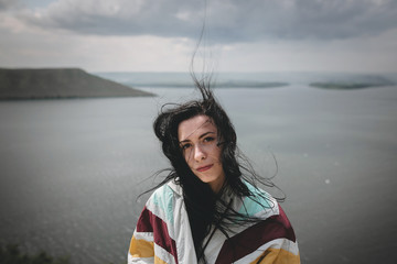 Stylish hipster girl with windy hair sitting on top of rock mountain with beautiful view on river. Young tourist woman relaxing on cliff. Atmospheric moment. Copy space