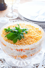 Layered salad with chicken and carrots in a crystal salad bowl on a white table, selective focus