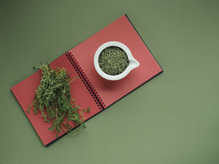 Ceramic white bowl of dry thyme (thymus serpyllum) on green and red background.