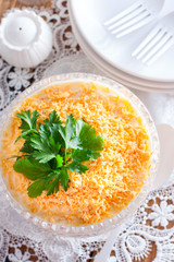Layered salad with chicken and carrots in a crystal salad bowl on a white table, selective focus