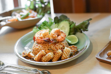 Spicy seafood fried rice. Thai street food of fried rice spicy seafood with soft focus on the giant shrimps, blurred background of thai papaya salad or som tam.