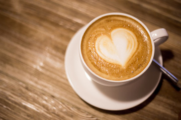 White cup of coffee with heart art on wooden table background