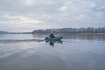Fishing. Fisherman on inflatable boat with fishing tackle at lake in winter.