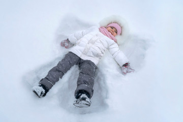 Cute girl child makes snow angel at winter park