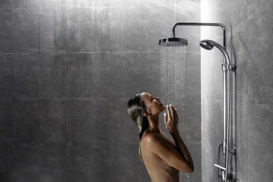 Woman taking shower in dark modern bathroom interior