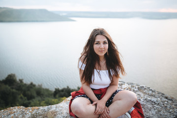 Hipster girl with windy hair sitting and meditating on top of rock mountain with beautiful view on...