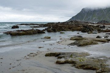 Beautiful nature landscape in North. Scenic outdoors view. Ocean with waves and mountains. Big dark stones. Dramatic storm clouds. Extreme weather, rain and wind. Explore Norway, summer adventure