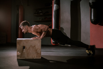 Young guy with a perfect body in a cross fitness class doing push-ups over the wooden box...