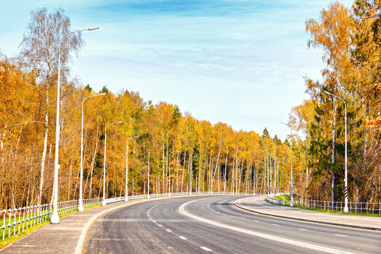 golden autumn road forest landscape on sunny day against blue sky background street view of modern 4 lane freeway with pedestrian and bike path and light poles in moscow russia vintage stylized photo