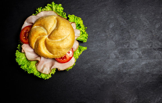 complete deli sandwich filled with ham slices salad and tomato over dark background with copy space
