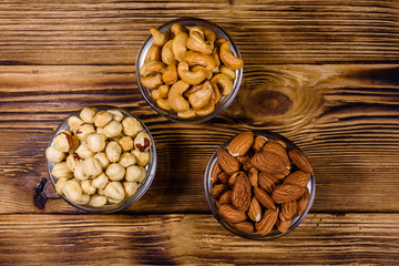 Various nuts (almond, cashew, hazelnut) in glass bowls on a wooden table. Vegetarian meal. Healthy eating concept. Top view