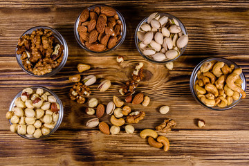 Various nuts (almond, cashew, hazelnut, pistachio, walnut) in glass bowls on a wooden table. Vegetarian meal. Healthy eating concept. Top view