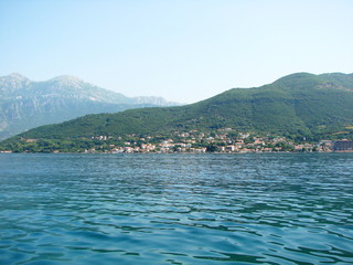 Fototapeta premium Landscape of the mirror blue surface of the Gulf reflecting coastal settlements against the backdrop of green hills and clear skies.