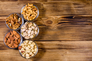 Various nuts (almond, cashew, hazelnut, pistachio, walnut) in glass bowls on a wooden table. Vegetarian meal. Healthy eating concept. Top view