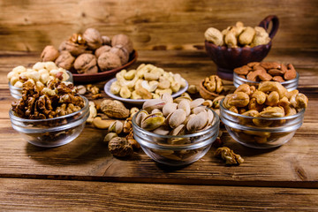 Various nuts (almond, cashew, hazelnut, pistachio, walnut) in bowls on a wooden table. Vegetarian meal. Healthy eating concept