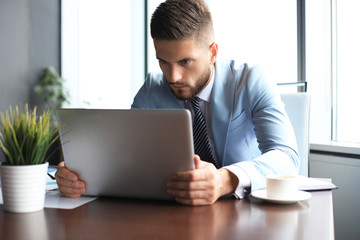 Fototapeta premium Good looking business man is holding laptop while sitting in the office