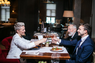 Happy business partners cheerfully raising hands with glasses of wine, gladly congratulate each other with successful deal, posing in luxury restaurant