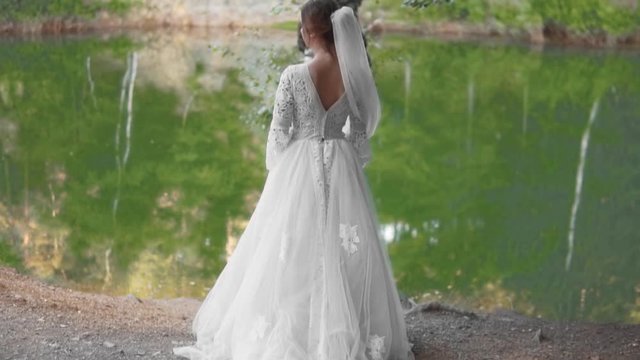 Bride in a wedding dress are standing near the river and posing for a photo.
